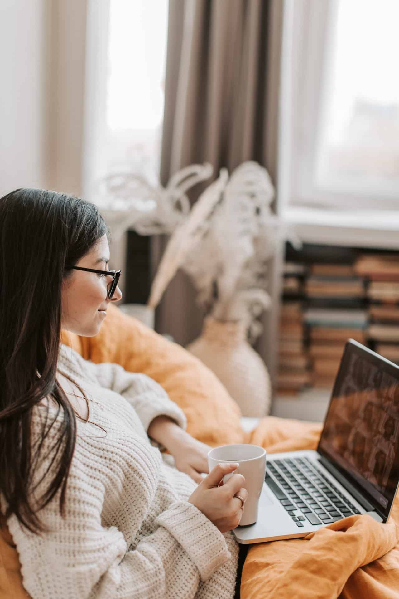 Woman attends an online therapy session on her laptop from her sofa. Her posture is relaxed and comfortable.
