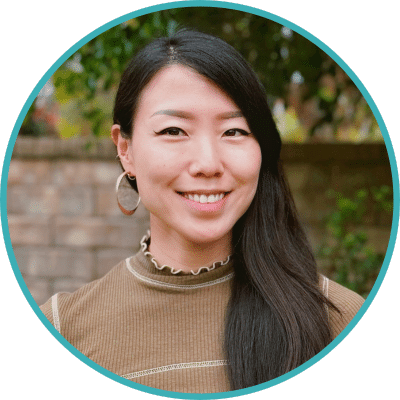 Circle headshot of Esther Kwon, an Asian American woman with long dark hair, wearing a brown top and gold hoop earrings. Esther appears to be outdoors in a park-like setting and is smiling.